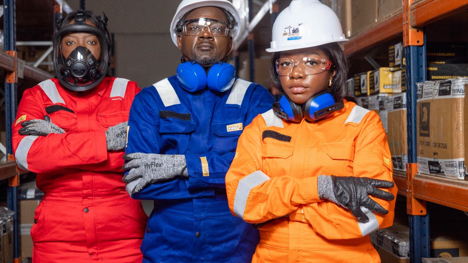 Three RIGSTOCK professionals in personal protective equipment — coveralls, helmets, goggles, gloves and a respirator — in a warehouse.